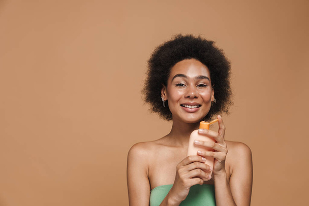Black brunette woman smiling while posing with beauty product isolated over beige background - Foto, immagini