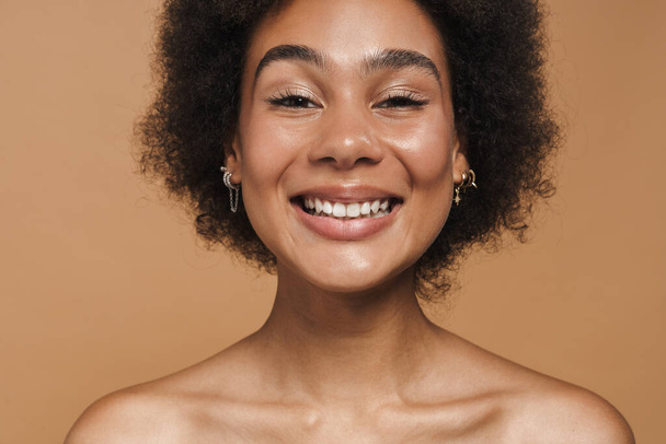 Black curly shirtless woman laughing and looking at camera isolated over beige background - Foto, Imagem
