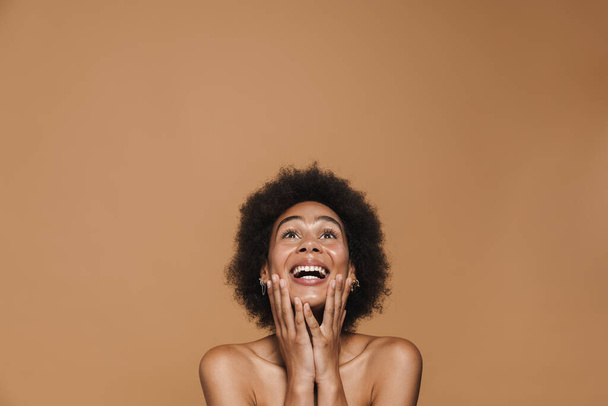 Black shirtless woman expressing surprise and looking upward isolated over beige background - Foto, immagini