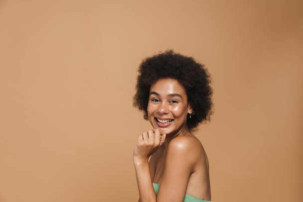 Black brunette curly woman smiling and looking at camera isolated over beige background - Foto, afbeelding