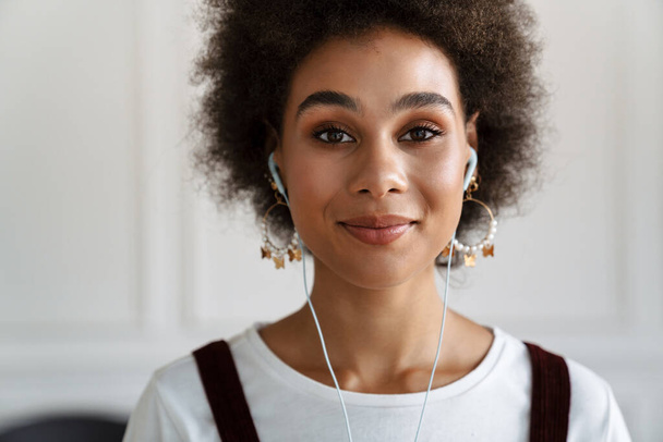 Black young woman smiling while listening music with earphones indoors - Foto, immagini