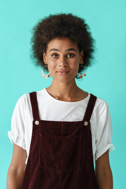 Black young woman in earrings posing and looking at camera isolated over blue background - Foto, afbeelding