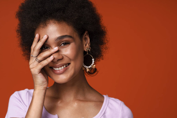 Young black woman wearing earrings smiling and covering her face isolated over brown background - Fotoğraf, Görsel