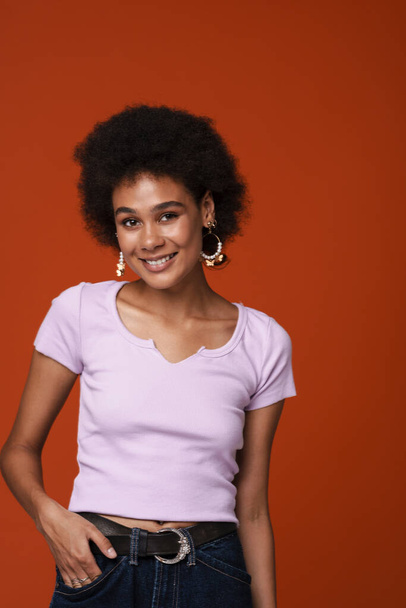 Black young woman in earrings smiling and looking at camera isolated over brown background - Photo, Image