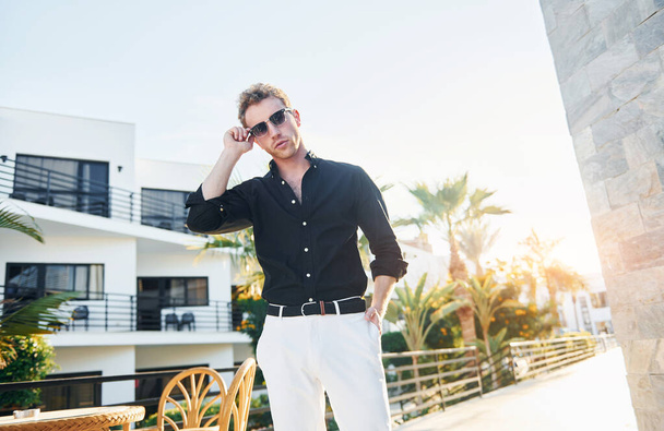 In sunglasses. Young man is outdoors at sunny daytime. Concept of vacation. - Photo, image