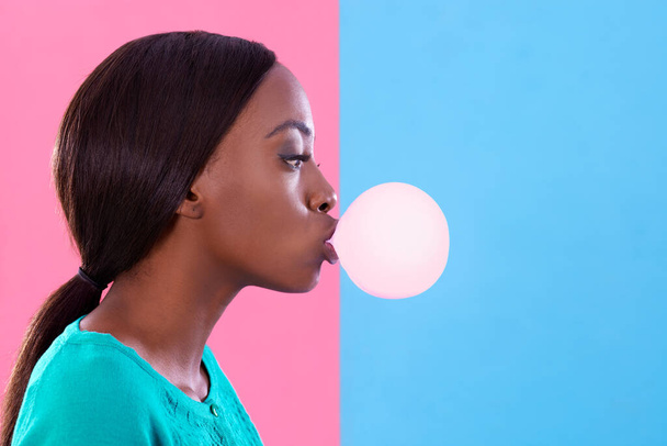 Bubblicious. Studio shot of an attractive young woman blowing a gum bubble against a colorful background. - Foto, Imagen