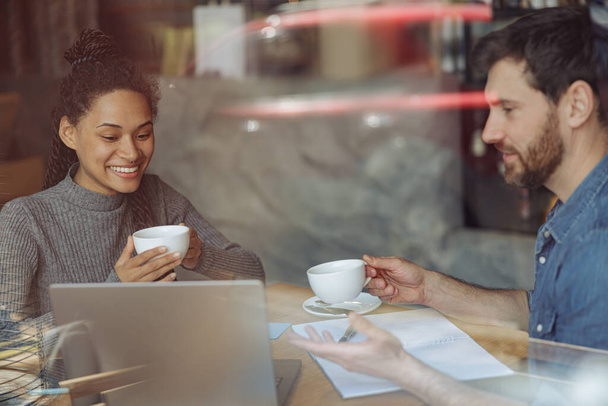 Joyeux couple de startupers souriant et buvant du café dans le café. Amis avec des tasses à ordinateur portable. - Photo, image