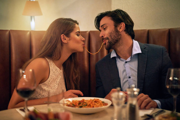Nada inspira un romance como la comida italiana. Foto de una joven pareja compartiendo espaguetis durante una cena romántica en un restaurante. - Foto, Imagen
