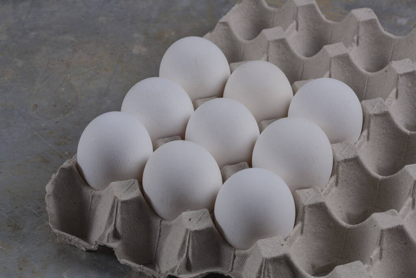 Курячі яйця крупним планом в кортонній коробці на сірій підставці
 - Фото, зображення