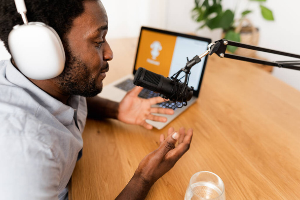 Afrikaanse man die een podcast opneemt met microfoon en laptop uit zijn thuisstudio - Foto, afbeelding