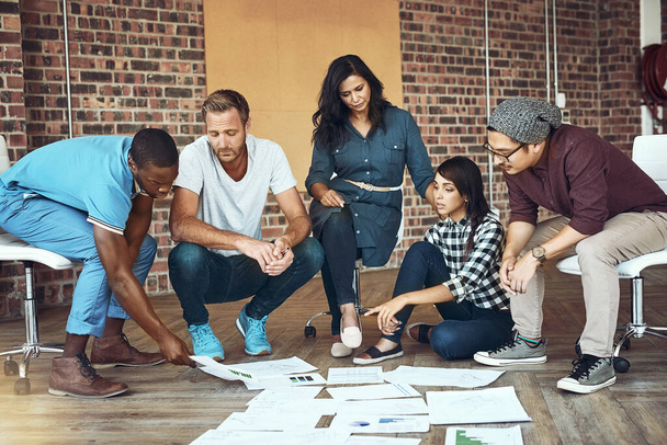 Schwierig wird leicht, wenn man ein tolles Team hat. Aufnahme eines Teams von Unternehmern, die auf dem Boden in einem modernen Büro zusammenarbeiten. - Foto, Bild