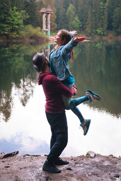 Beautiful couple of man and woman visiting an Carpathians lake Synevyr, Ukraine - Tourists having fun on vacation Concepts about travel, lifestyle and wanderlust. happy warm hugs. Vertical photo - Foto, immagini