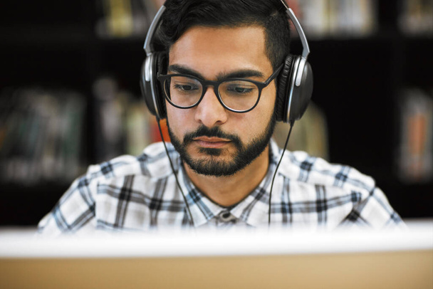 Vai ser um longo dia para mim. Foto de perto de um jovem focado sentado e trabalhando em um computador em uma biblioteca enquanto ouve música. - Foto, Imagem