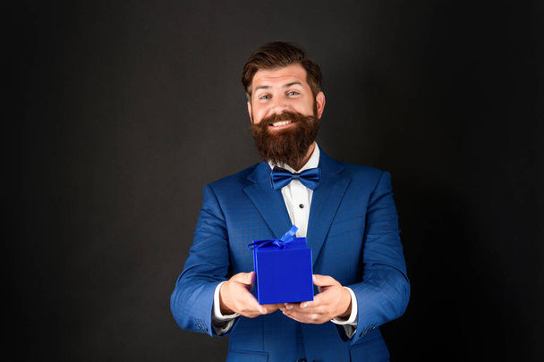 happy man in tuxedo bow tie formalwear on black background presenting box. shopping sale - Foto, Bild