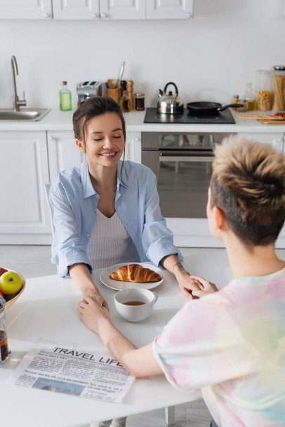 bigender couple holding hands near breakfast and travel life newspaper in kitchen - Photo, Image