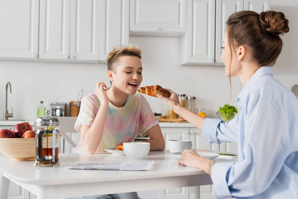bigender person feeding lover with tasty croissant during breakfast - Foto, immagini