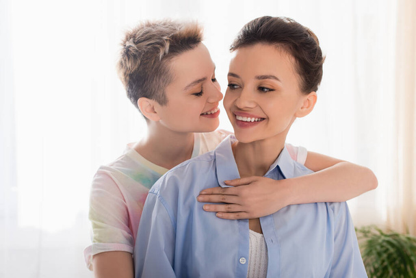 young bigender person with closed eyes embracing smiling partner - Foto, afbeelding