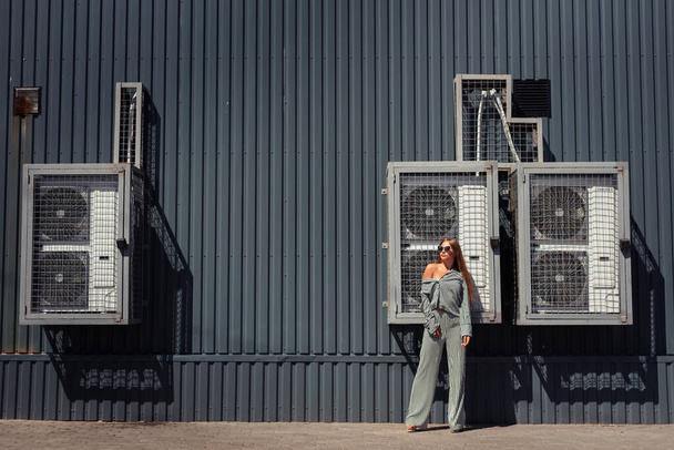 A girl in a striped suit stands against the backdrop of a factory, fans. The girl looks away. Free space for text. - Foto, Imagem