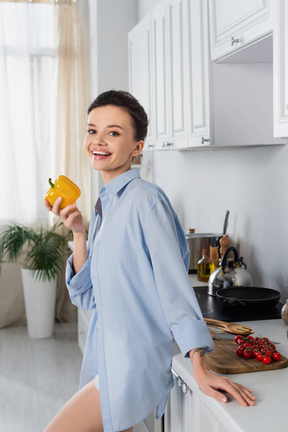 smiling woman holding bell pepper and looking at camera near fresh cherry tomatoes - Fotoğraf, Görsel
