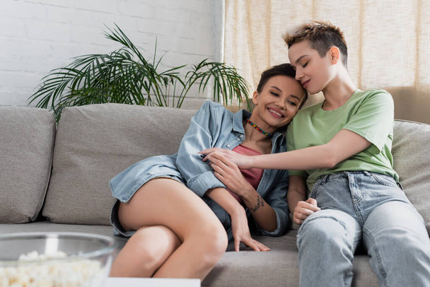 young bigender person with closed eyes sitting on sofa near cheerful partner - Foto, Bild
