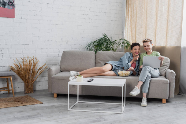 cheerful pangender lovers watching movie on laptop in modern living room - Valokuva, kuva