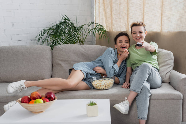 laughing pansexual couple watching movie on tv near popcorn and fresh apples - Fotó, kép