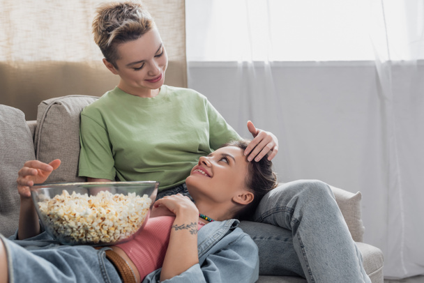 young bigender partner touching head of happy lover lying on couch with popcorn - Photo, image