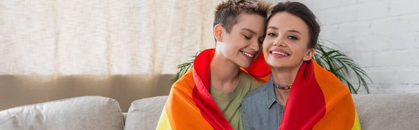 cheerful pansexual couple covered with lgbt flag smiling at home, banner - Photo, Image