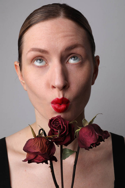 Portrait of young woman with dry roses and funny face grimace. Vertical. - Fotografie, Obrázek