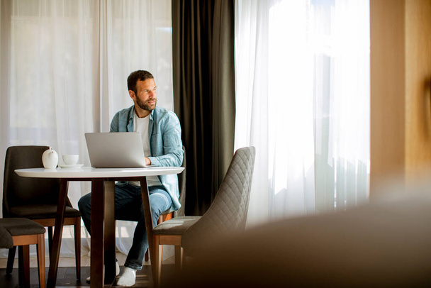 Красивый молодой человек с ноутбуком и пить чай в гостиной - Фото, изображение