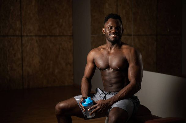 Shirtless african american man drinking from a shaker in the gym. - Fotoğraf, Görsel
