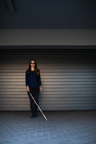 Blinde vrouw die door de straten van de stad loopt, haar witte stok gebruikt om beter door de stedelijke ruimte te navigeren en veilig op haar bestemming te komen - Foto, afbeelding