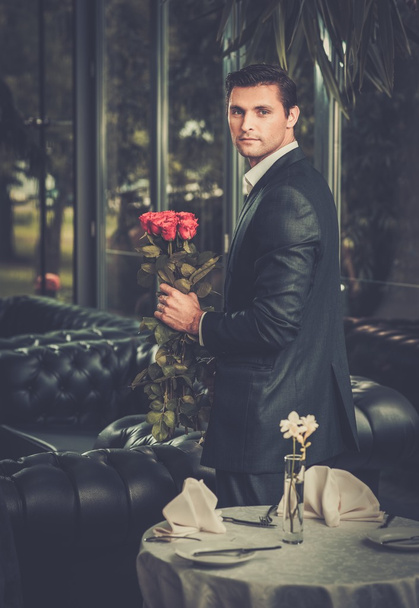 Bonito homem com um monte de rosas vermelhas esperando sua senhora no restaurante
  - Foto, Imagem