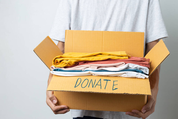 Donation Concept, man holding clothes with donate box in white background room. - Фото, изображение