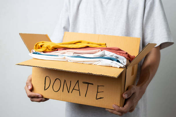 Darování Koncept, muž drží oblečení s dárcem box v bílém pozadí místnosti. - Fotografie, Obrázek