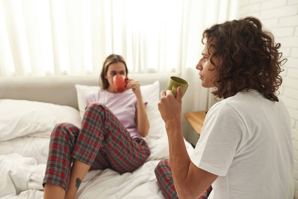 Thoughtful guy drinking tea with girlfriend on bed - 写真・画像