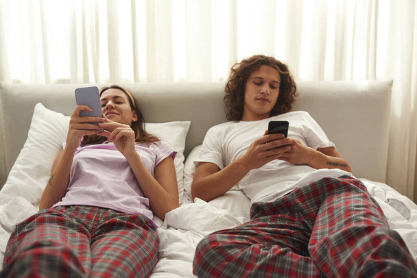 Couple lying and using smartphones on bed at home - Valokuva, kuva