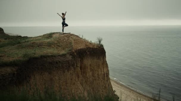 Plaj tepesinde yoga ağacı pozu veren bir kız. Bir bacağı açık havada duran bir kadın. - Video, Çekim