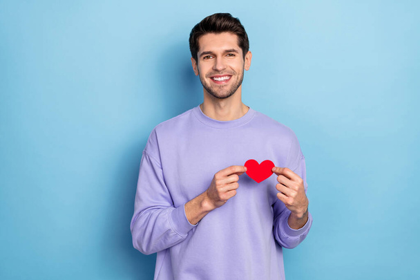 Photo of nice millennial brunet guy hold heart wear sweater isolated on blue color background - Photo, Image