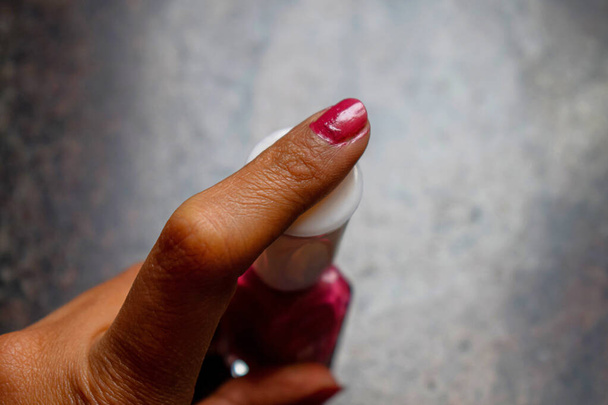 top view of a girl hand holding dark pink color nail paint bottle and showing her index fingers nail painted with dark pink color nail paint. Picture captured under natural light at Bangalore, India. - Foto, Imagen
