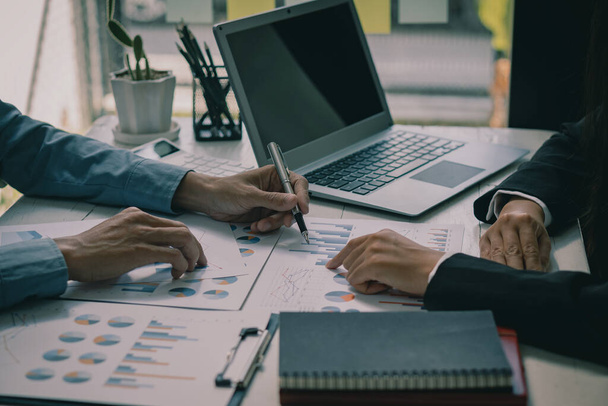 Close-up of two businessmen with pens pointing to graphs while chatting on wooden table with laptop, teamwork discussing up and down financial accounts, market economy. - Foto, Imagen