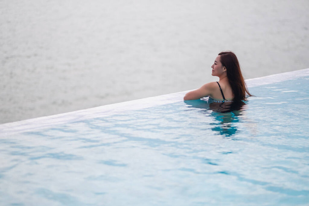 Uma jovem mulher asiática relaxante na piscina infinita olhando para uma bela vista mar - Foto, Imagem