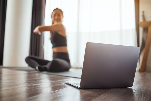 Eine junge Frau breitet die Arme aus, während sie zu Hause Online-Workout-Tutorials am Laptop anschaut - Foto, Bild