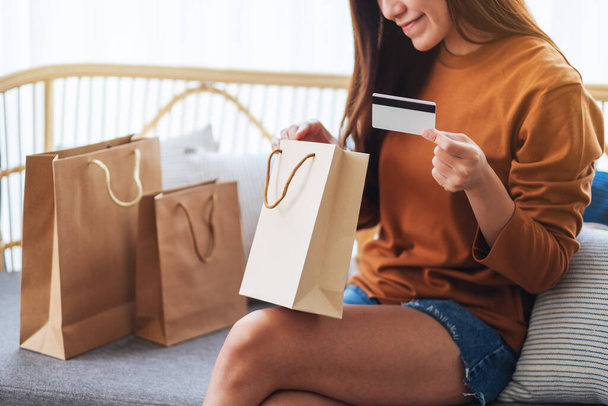 Imagen de primer plano de una hermosa mujer joven con tarjeta de crédito mientras abre bolsas de compras en casa - Foto, imagen