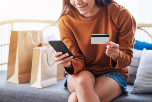 Closeup image of a beautiful young woman using mobile phone and credit card for online shopping - 写真・画像
