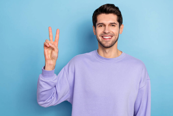 Photo of cool millennial brunet guy show v-sign wear sweatshirt isolated on blue color background - 写真・画像