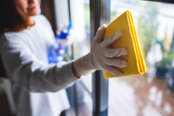Een jonge vrouw met beschermende handschoen die het raam schoonmaakt voor huishoudelijk werk - Foto, afbeelding