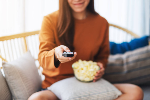 Nahaufnahme einer Frau, die Popcorn isst und Kanäle mit Fernbedienung sucht, um fernzusehen, während sie zu Hause auf dem Sofa sitzt - Foto, Bild