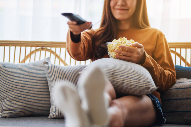 Zbliżenie obraz kobiety jedzącej popcorn i kanał wyszukiwania z pilotem do oglądania telewizji podczas siedzenia na kanapie w domu - Zdjęcie, obraz