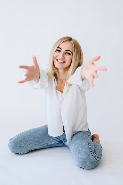 The blonde girl smiles broadly and stretches with outstretched arms on a white background. Concept: go, I'll hug you. - Photo, image